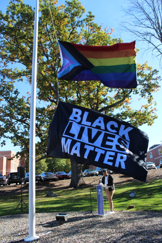 LGBTQ and Black Lives Matter flags blow with student in background