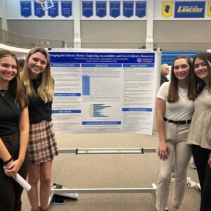 Two students stand on each side of a board with information on their research.