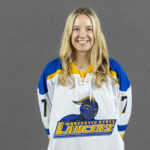 Female student in athletic jersey stands and smiles