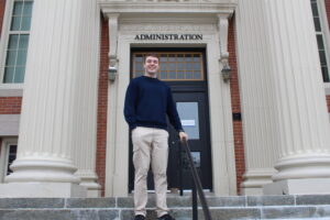 A person stands on steps in front of a building labeled "Administration," with large columns and a black door in the background.