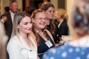 Three women with name tags smiling at a social gathering.