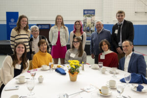 A group of people sitting at and standing behind a round table during a Worcester University event.
