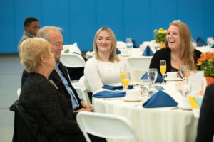 Four people seated around a circular banquet table during an event, with the woman on the right laughing.