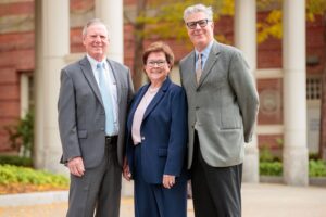 Three people in business attire standing outdoors in front of a brick building.