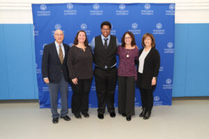 Five people posing for a photo in front of a blue Worcester University backdrop.