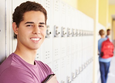 Latino student standing in front of lockers in a hallway.