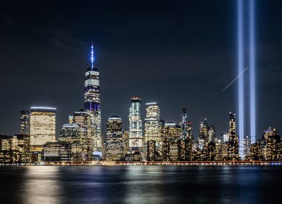 New York City skyline at night, with buildings lit up and the lights from the 9/11 Memorial going up into the sky