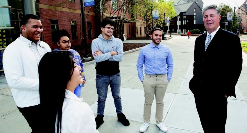 Group of students stand in circle talking to university president