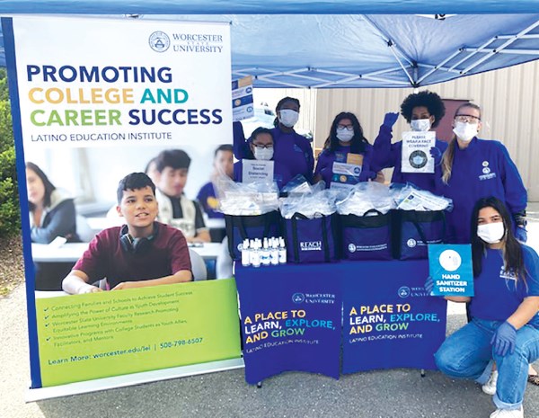 Students wearing masks surround a table covered with bags of health materials next to a banner: Promoting College and Career Success