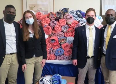 4 students wearing mask standing in from of table piled with rolled up blankets