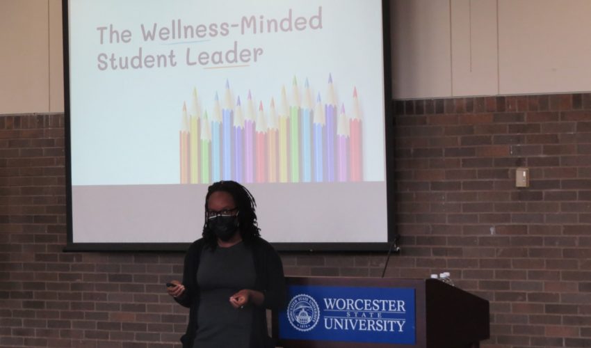 Amma Marfo stands by a podium, in front of a screen that says The Wellness-minded Student Leader