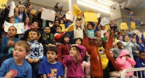 School children cheering in indoor basketball court bleachers
