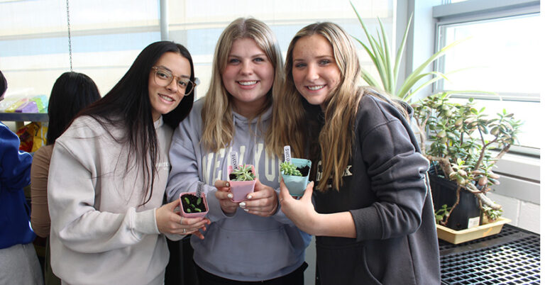 Three female students holding potted plants