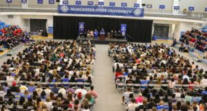 Large gymnasium full of students facing a podium with a faculty speaker