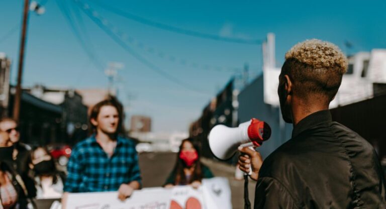 Person holding megaphone faces into a crowd with two people holding a banner