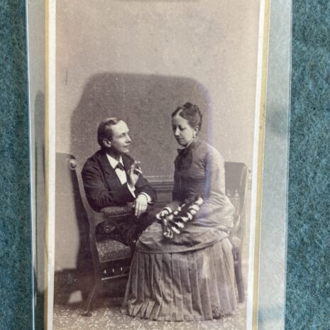 Two people in Victorian clothing sit close together, facing each other and signing