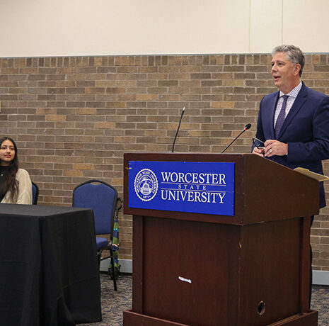 A man speaks at a podium labeled 