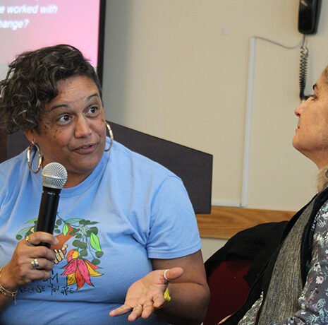 Two women are engaged in conversation in front of a Worcester State University podium; one gestures while speaking.