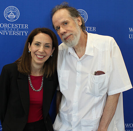 Two people stand in front of a blue Worcester State University backdrop, smiling at the camera.