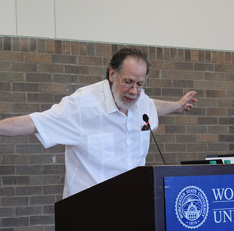 A man in a white shirt speaks at a podium with 