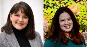 Two women smiling; the left woman has shoulder-length dark hair, wears a gray blazer and black turtleneck, and the right woman has long brown hair, wearing a green top with plants in the background.
