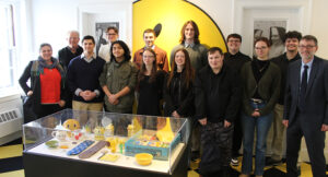 A group of people pose for a photo in a brightly lit room with a yellow and black decor, standing behind a display case filled with various yellow-themed objects.