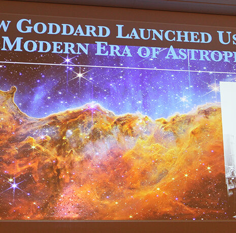 Presentation slide titled "How Goddard Launched Us into the Modern Era of Astrophysics" with a space nebula image and a black-and-white photo of a man with a rocket.