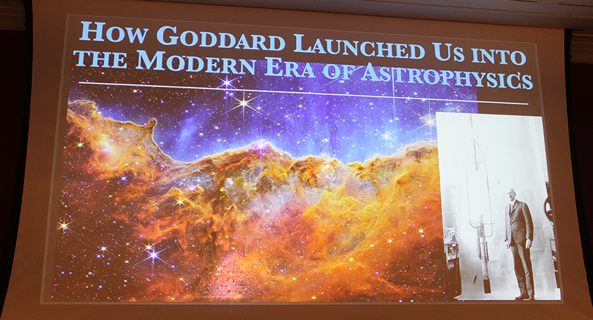Presentation slide titled "How Goddard Launched Us into the Modern Era of Astrophysics" with a space nebula image and a black-and-white photo of a man with a rocket.