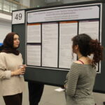 Two women stand in front of a scientific poster titled "A Java Based Pet Adoption Center System Using Data Structures for System Efficiency & Optimization" at a presentation event.