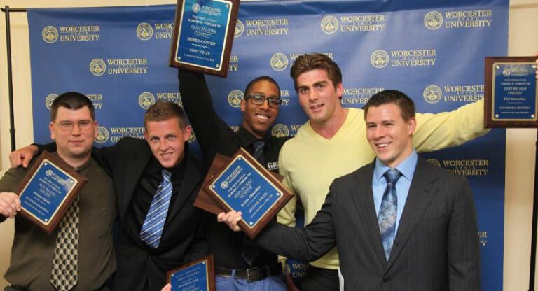 Five men pose in front of a Worcester University backdrop, each holding a plaque and smiling for the camera.