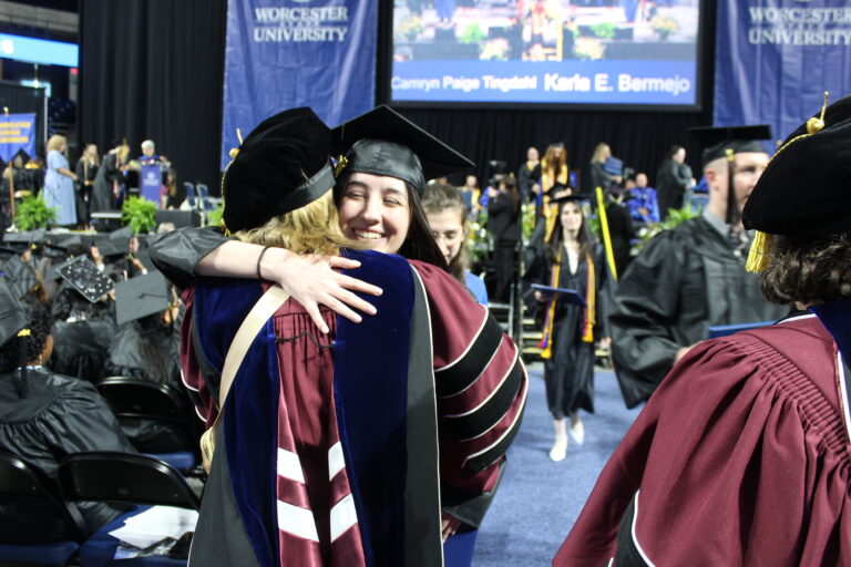 Graduates in cap and gown hug.
