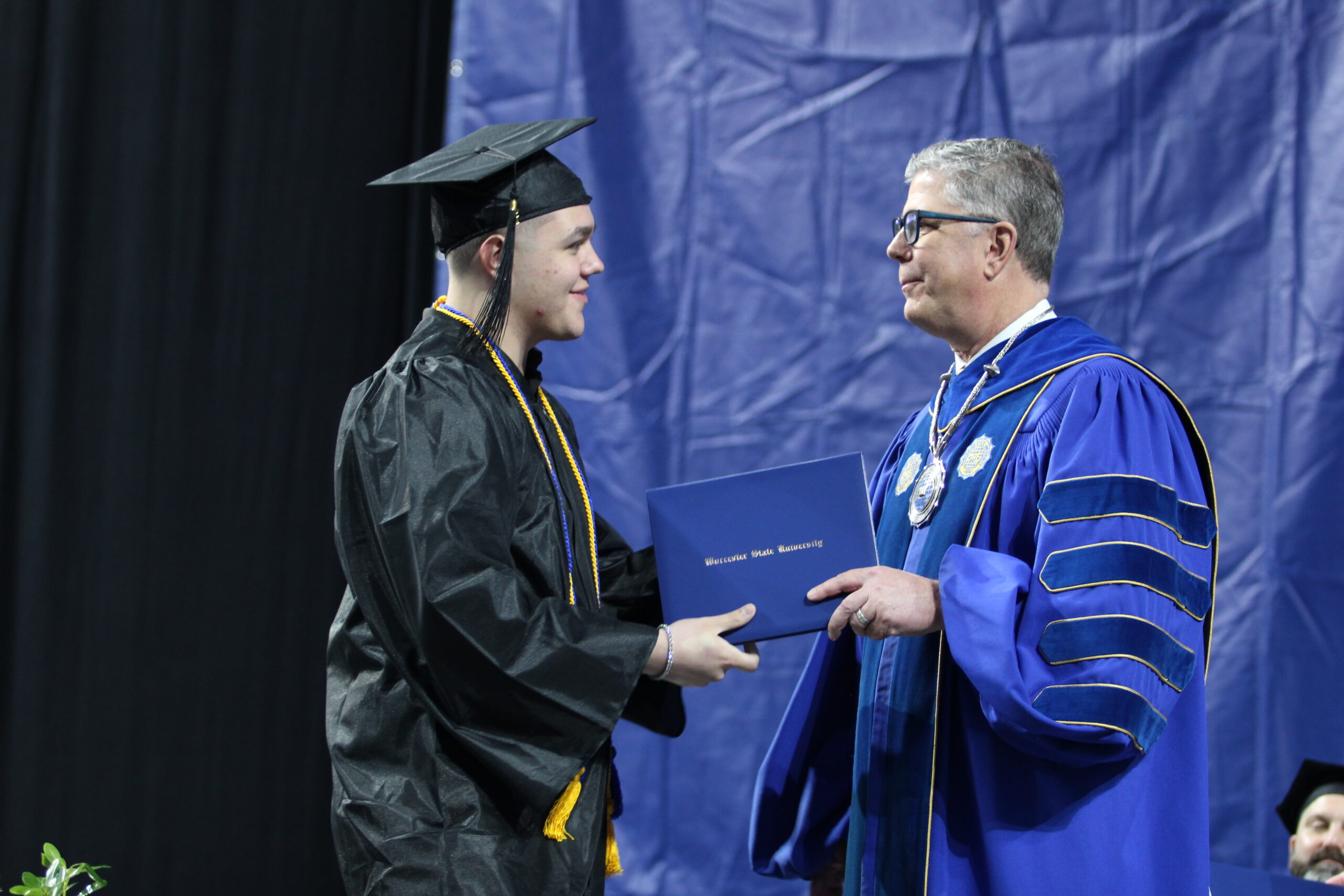 A graduate in a cap and gown receives a diploma from a man in academic regalia during a graduation ceremony.