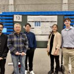 Five people stand in front of a scientific poster presentation at an indoor venue with blue bleachers in the background. The poster board displays research on protein kinase inhibitors.