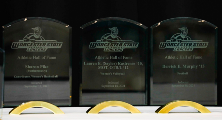 Three Worcester State Lancers Athletic Hall of Fame plaques for Sharon Pike, Lauren E. Kastrenos, and Derrick E. Murphy, displayed side by side on a table.