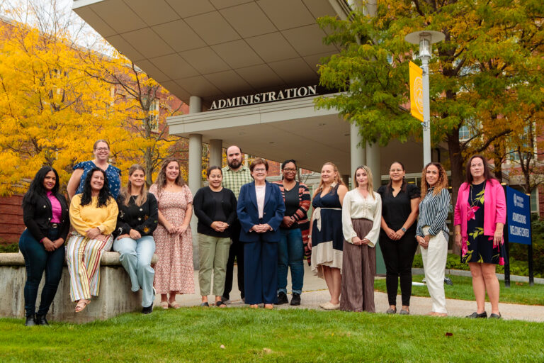 A group of thirteen people standing in front of an administration building.