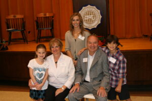 A multi-generational group of four people posing for a photo in front of a Worcester State University emblem on a stage.