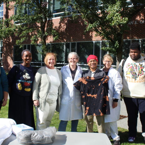 A group of students and faculty members standing in front of a brick science building, with one person holding up a black tie-dye t-shirt.