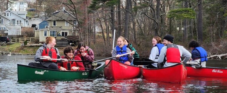A group of young people laughing while paddling in four canoes on a lake.